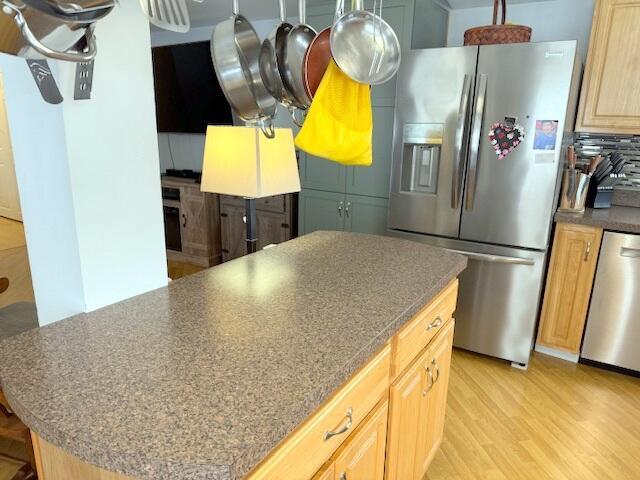 kitchen featuring dark countertops, backsplash, a center island, light wood-type flooring, and appliances with stainless steel finishes