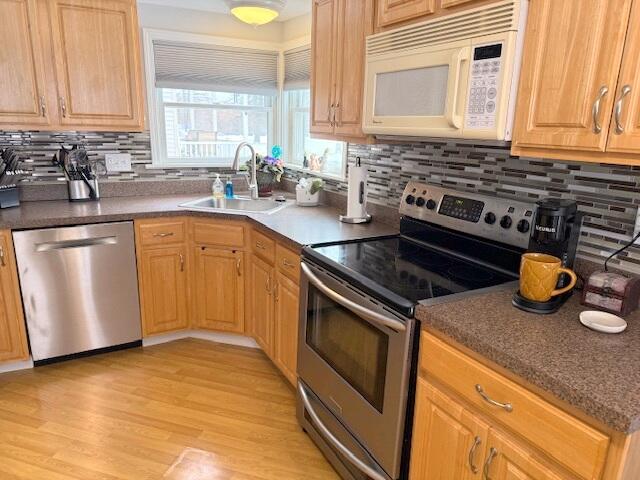 kitchen featuring decorative backsplash, light wood-style flooring, appliances with stainless steel finishes, and a sink