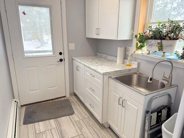 clothes washing area featuring baseboard heating, plenty of natural light, and a sink