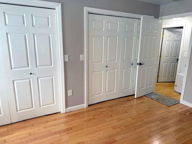 unfurnished bedroom with baseboards, light wood-style floors, and multiple closets