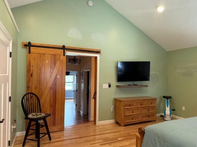 bedroom featuring light wood finished floors, baseboards, high vaulted ceiling, and a barn door