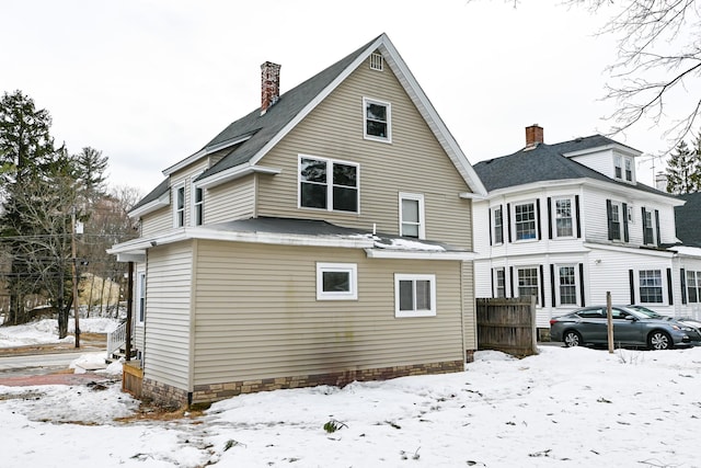 snow covered rear of property featuring fence and a chimney