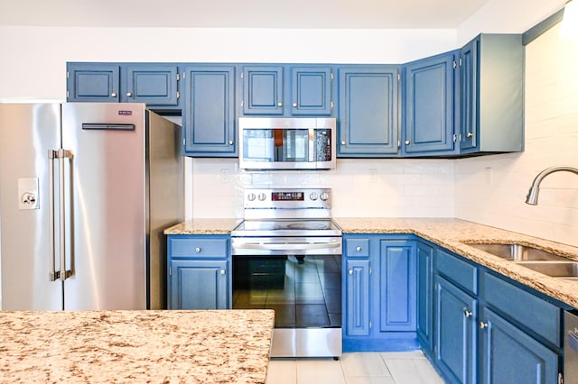 kitchen featuring tasteful backsplash, blue cabinetry, light stone counters, stainless steel appliances, and a sink