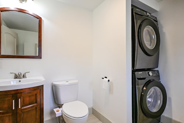 half bathroom with vanity, toilet, stacked washer / drying machine, and baseboards