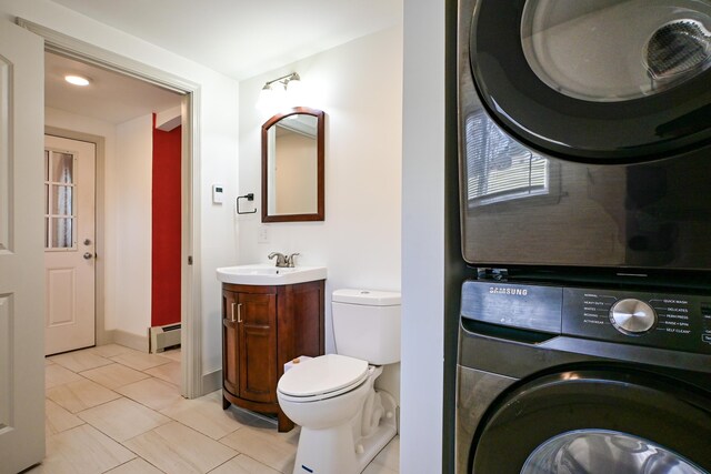 bathroom featuring stacked washer and dryer, toilet, a baseboard heating unit, tile patterned flooring, and vanity