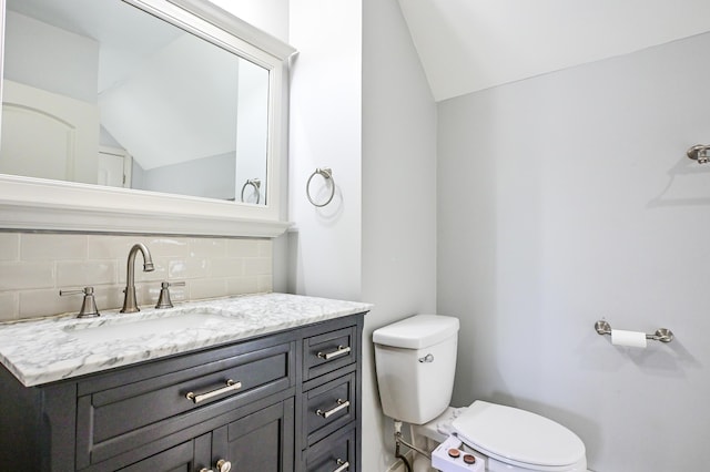 half bathroom with tasteful backsplash, toilet, vanity, and vaulted ceiling