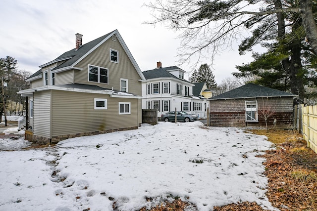 snow covered property with an outbuilding, a chimney, and fence