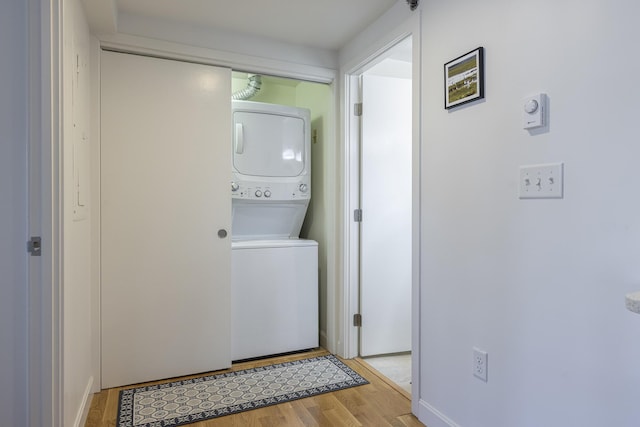 clothes washing area featuring laundry area, stacked washer and dryer, and light wood finished floors