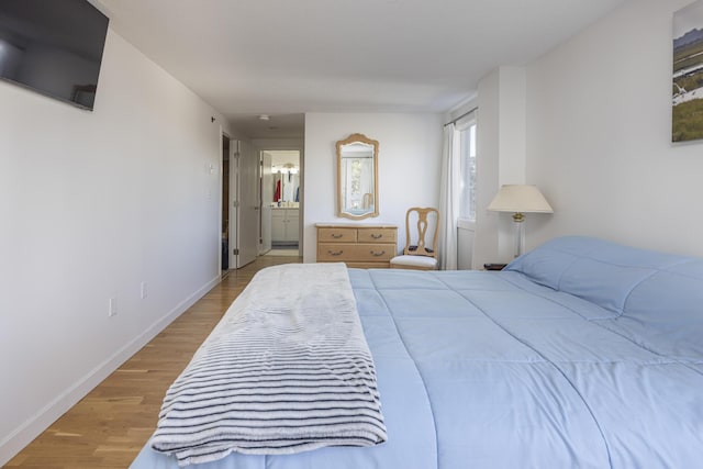 bedroom with ensuite bath, baseboards, and wood finished floors