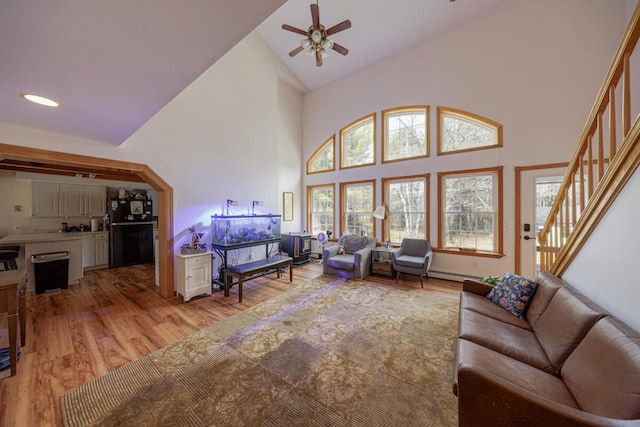 living room with high vaulted ceiling, light wood-style flooring, a ceiling fan, stairway, and a baseboard radiator