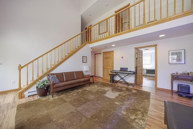 living area with wood finished floors, baseboards, a baseboard radiator, stairs, and a towering ceiling