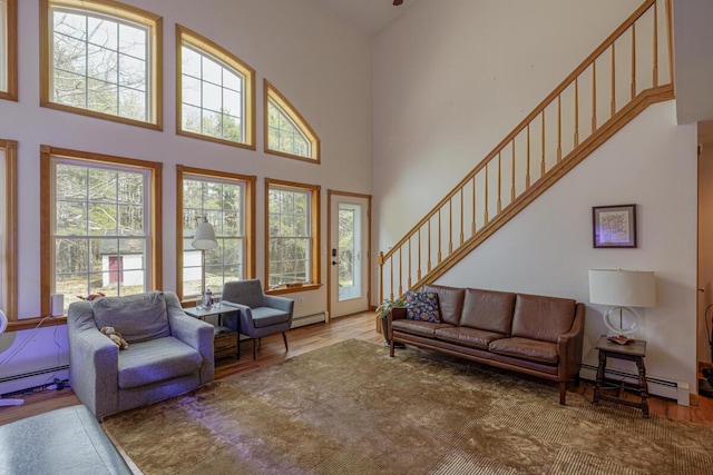 living area featuring stairway, wood finished floors, a high ceiling, and a baseboard radiator