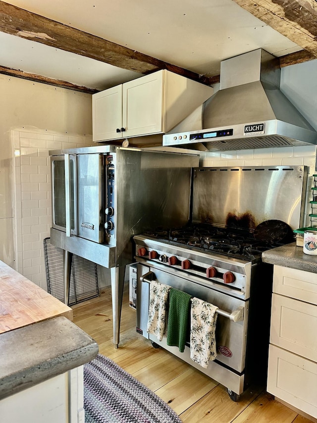 286 Lexington Rd, Kingfield, ME 04947 - kitchen with wall chimney exhaust hood, high end stove, light wood-style flooring, beamed ceiling, and white cabinets