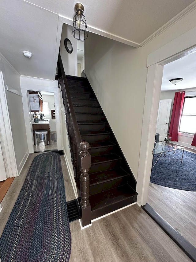 staircase featuring baseboards, wood finished floors, and ornamental molding