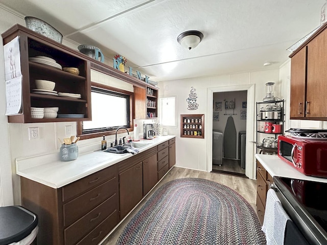 kitchen with open shelves, light countertops, light wood-style flooring, stainless steel range with electric cooktop, and a sink