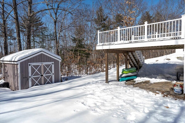 yard layered in snow with a wooden deck, an outbuilding, a storage shed, and stairs