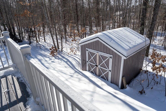 snow covered structure with an outbuilding, a storage shed, and a view of trees