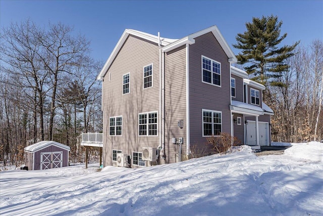 view of snowy exterior featuring an outdoor structure, an attached garage, and a shed