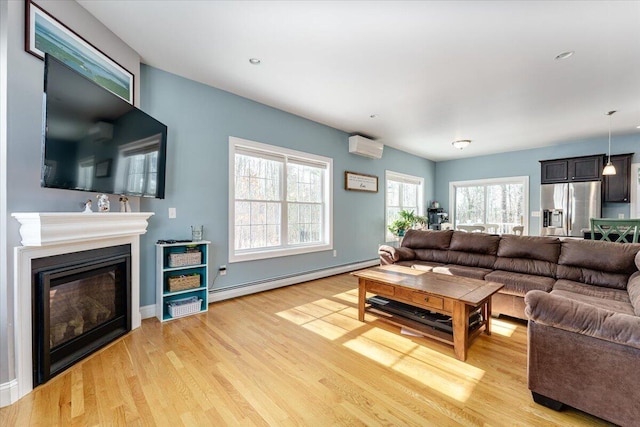 living room featuring a wall unit AC, a glass covered fireplace, baseboards, light wood finished floors, and a baseboard heating unit