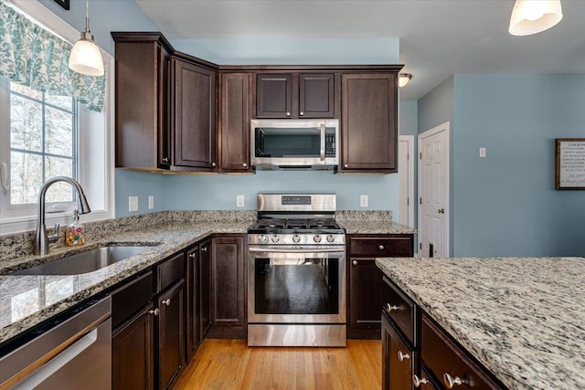 kitchen with light stone counters, light wood-style flooring, a sink, hanging light fixtures, and appliances with stainless steel finishes