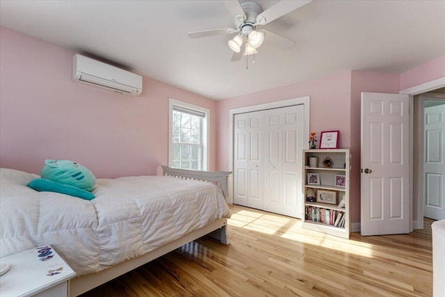 bedroom featuring a closet, a wall mounted air conditioner, light wood-type flooring, and ceiling fan