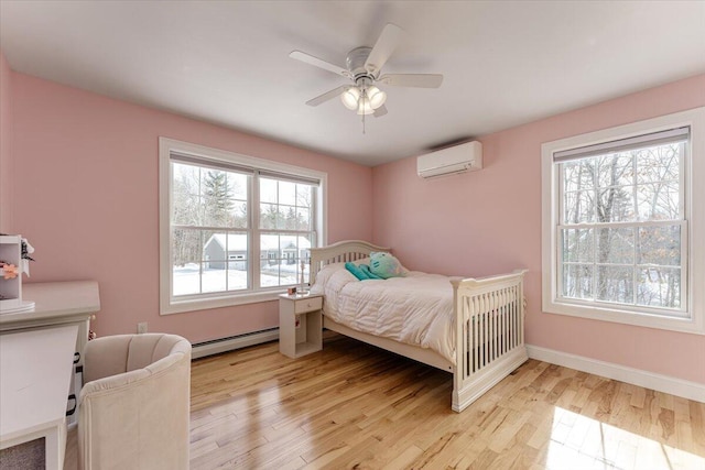 bedroom with a ceiling fan, a wall unit AC, light wood finished floors, baseboards, and baseboard heating