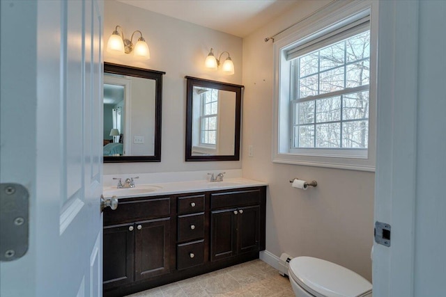 bathroom featuring double vanity, toilet, baseboards, and a sink