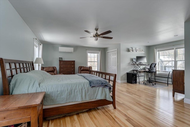 bedroom with multiple windows, wood finished floors, baseboards, and a wall mounted AC