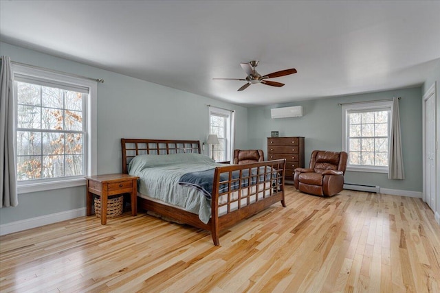 bedroom with a baseboard heating unit, ceiling fan, baseboards, an AC wall unit, and light wood-type flooring