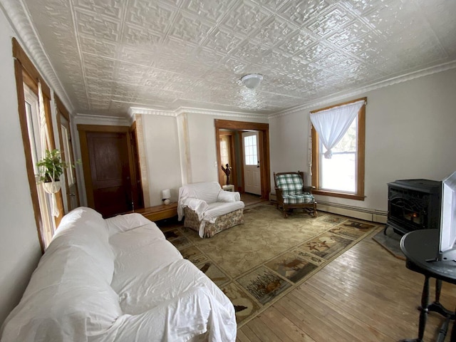 living room featuring hardwood / wood-style flooring, an ornate ceiling, crown molding, a baseboard radiator, and a wood stove