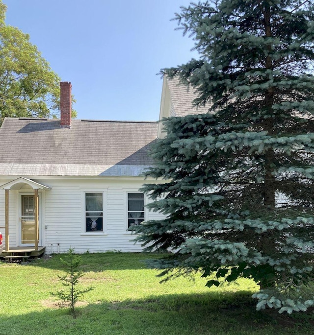 view of side of home featuring a yard, roof with shingles, and a chimney