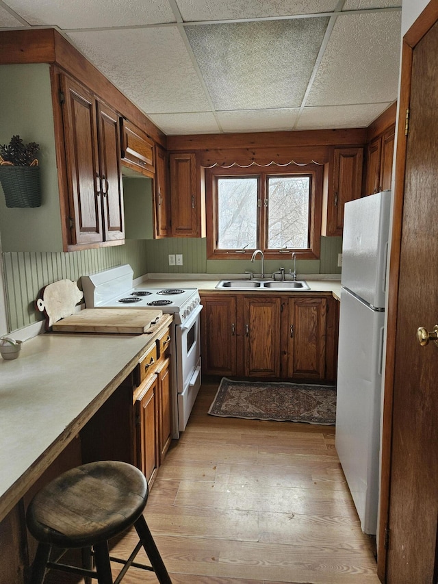 kitchen with a sink, white appliances, light countertops, and light wood finished floors