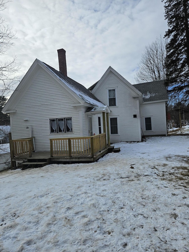 snow covered rear of property with a deck and a chimney