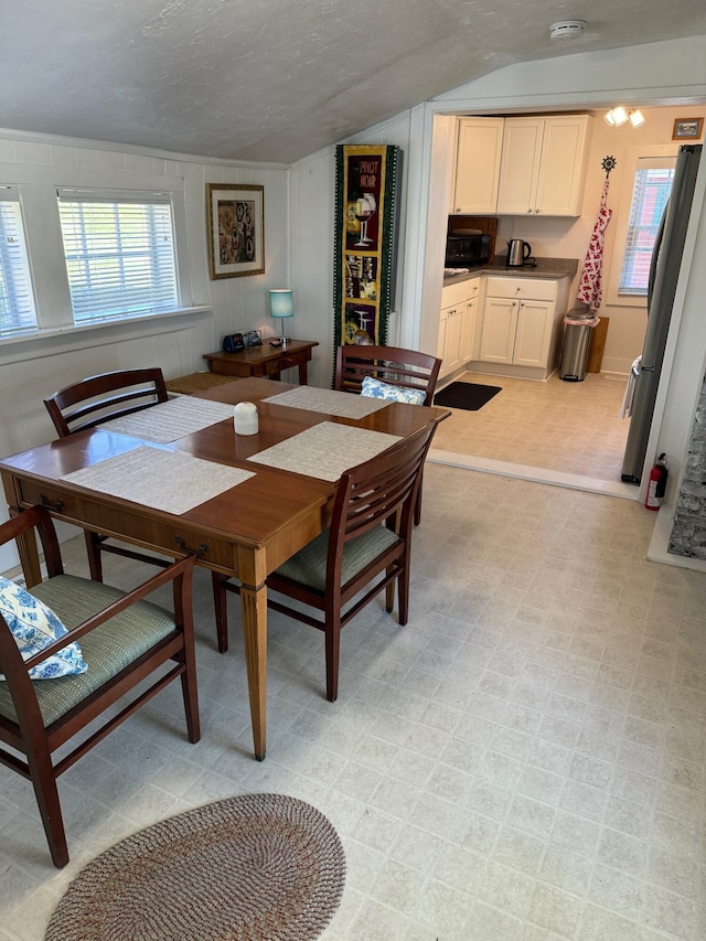 dining space with lofted ceiling, light floors, and a textured ceiling