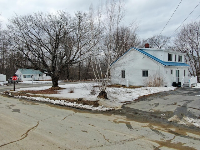 view of snow covered exterior featuring metal roof and a chimney