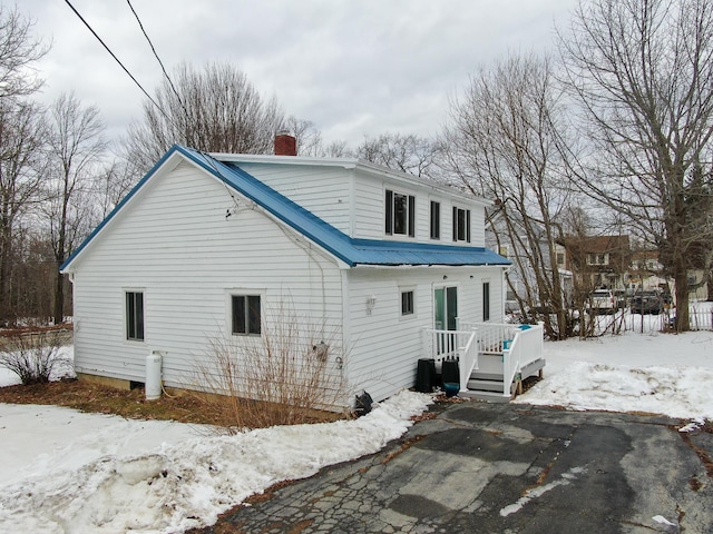 view of snow covered exterior featuring metal roof, a deck, and a chimney