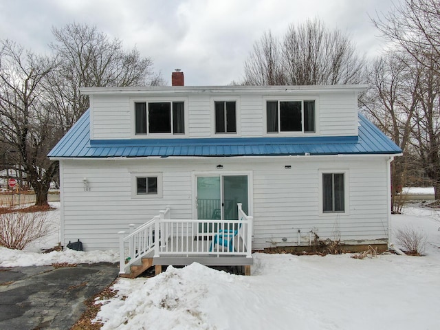 snow covered property with a chimney and metal roof