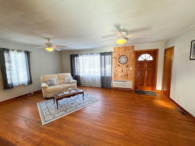 living area featuring a ceiling fan, wood finished floors, visible vents, baseboards, and an AC wall unit