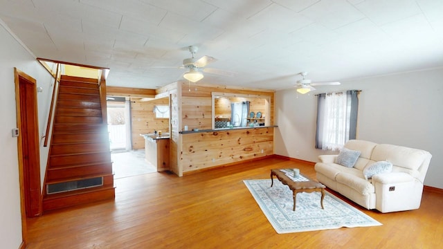 living room with wooden walls, ceiling fan, stairway, and light wood-style floors