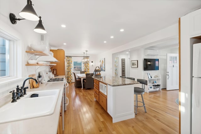 kitchen featuring open shelves, a breakfast bar area, a wall mounted air conditioner, white appliances, and a sink