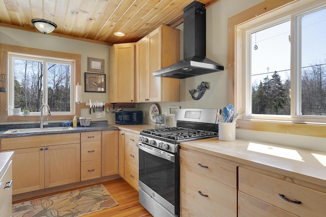 kitchen with light brown cabinetry, stainless steel range with gas cooktop, wall chimney exhaust hood, wood ceiling, and a sink