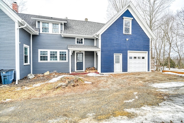 traditional-style house featuring an attached garage, driveway, roof with shingles, and a chimney