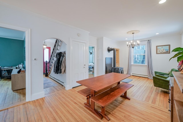 dining space featuring light wood finished floors, a baseboard radiator, a wood stove, arched walkways, and crown molding