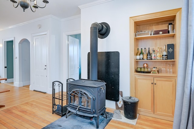 living room featuring a wood stove, arched walkways, light wood finished floors, and ornamental molding