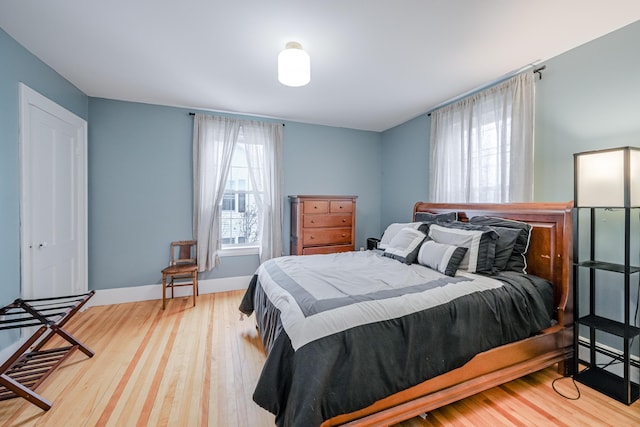 bedroom with multiple windows, wood finished floors, and baseboards