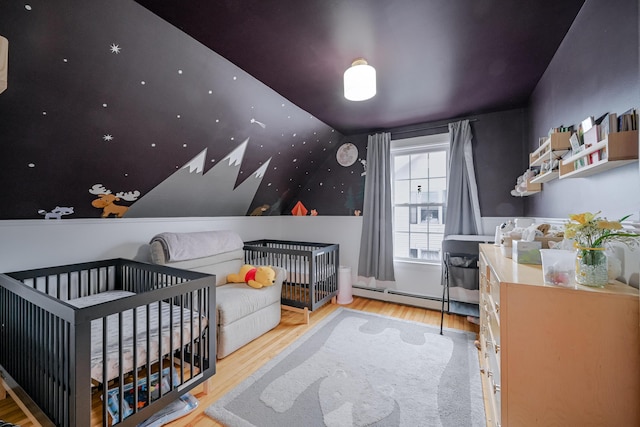 bedroom featuring a baseboard heating unit, a crib, and wood finished floors