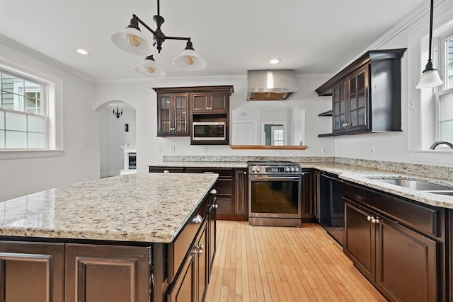 kitchen with dark brown cabinetry, wall chimney range hood, arched walkways, a sink, and stainless steel appliances