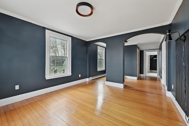 empty room featuring arched walkways, a baseboard radiator, baseboards, and light wood-style flooring