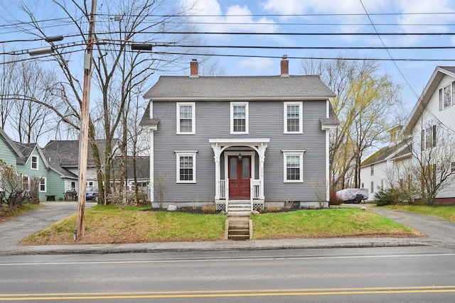 colonial home featuring a chimney, a shingled roof, and a front lawn