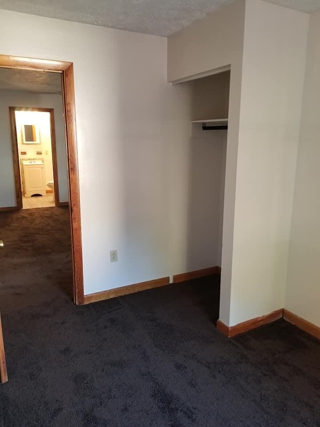 unfurnished bedroom with a closet, baseboards, a textured ceiling, and dark carpet